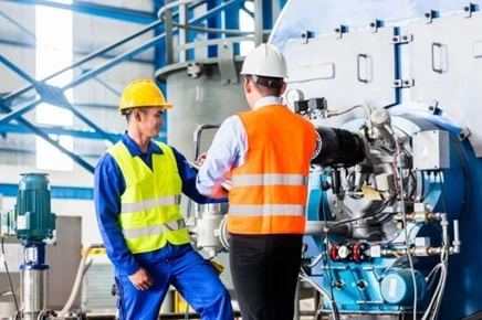 Hai công nhân mặc áo phản quang kiểm tra cụm bơm và đường ống trong nhà máy